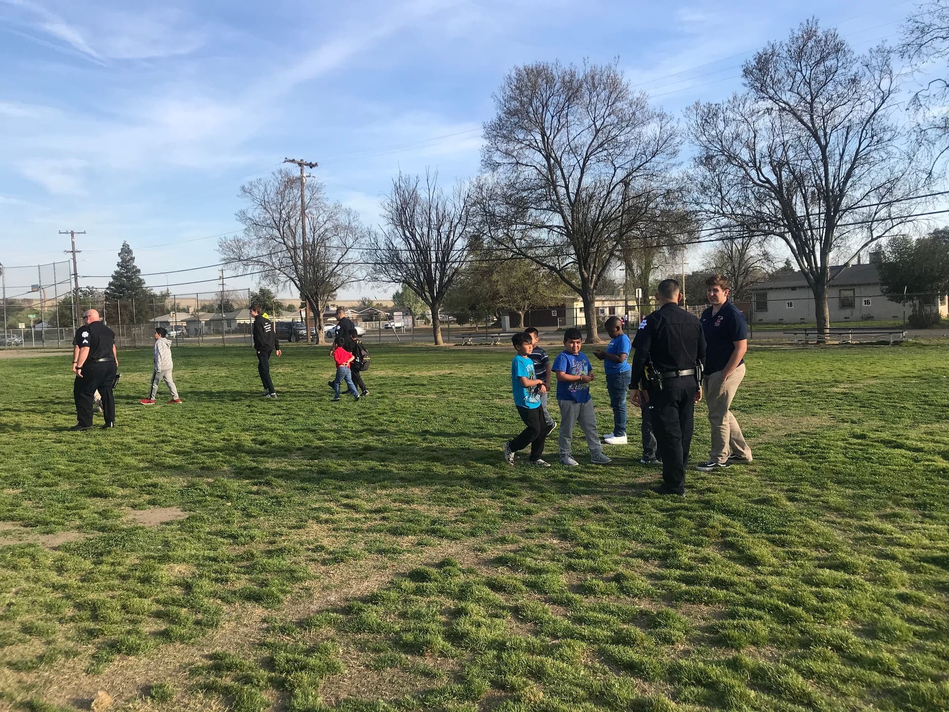 Mentors and officers walking with students on a Fresno school field